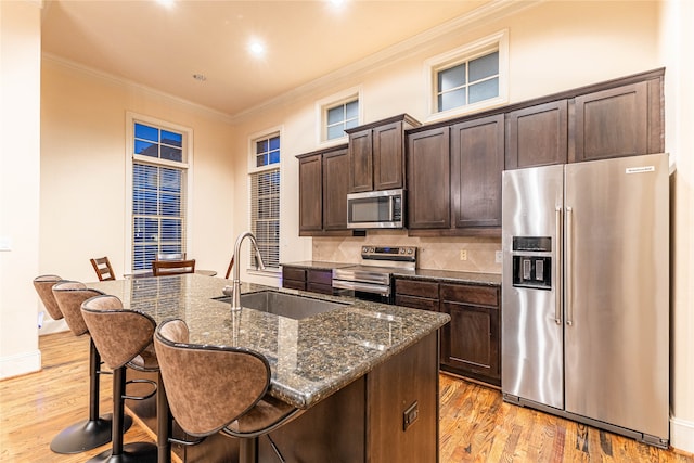 kitchen featuring appliances with stainless steel finishes, dark brown cabinetry, sink, dark stone countertops, and light hardwood / wood-style floors