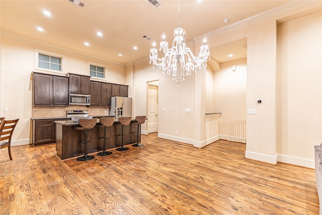 kitchen featuring an island with sink, light wood-type flooring, a breakfast bar, appliances with stainless steel finishes, and ornamental molding