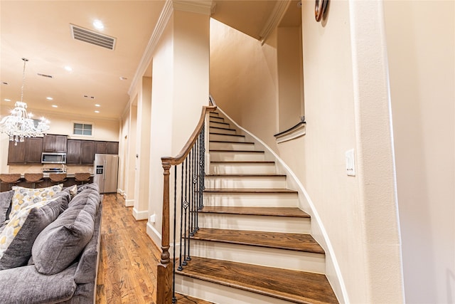 stairs featuring a chandelier, wood-type flooring, and ornamental molding