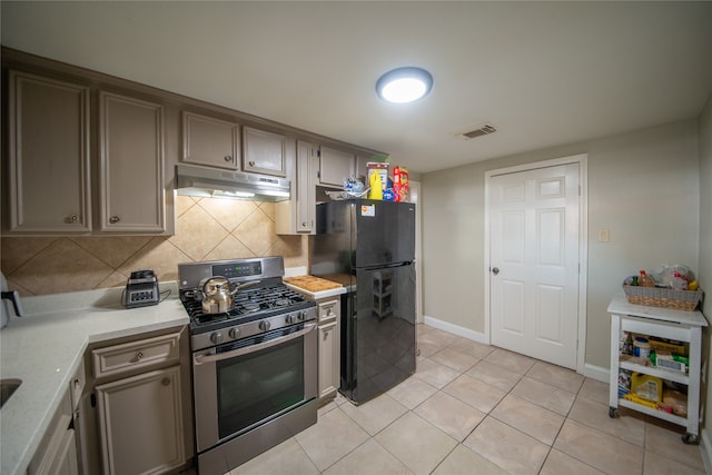 kitchen featuring decorative backsplash, light tile patterned floors, black fridge, and stainless steel gas range oven