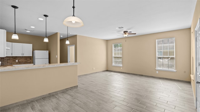 kitchen with white refrigerator, light wood-type flooring, pendant lighting, decorative backsplash, and white cabinetry