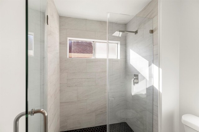 bathroom featuring a shower with door and toilet