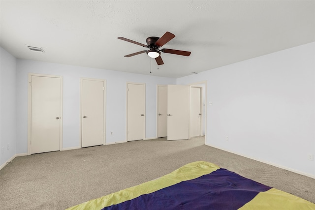 unfurnished bedroom with carpet flooring, ceiling fan, and multiple closets