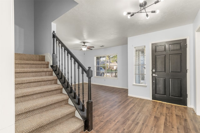 foyer featuring ceiling fan with notable chandelier, a textured ceiling, and dark hardwood / wood-style floors