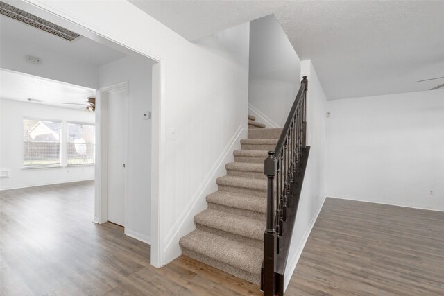 stairs with hardwood / wood-style floors, a textured ceiling, and ceiling fan