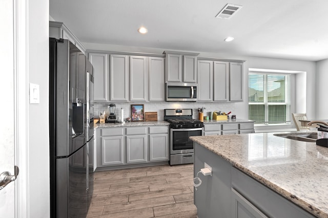 kitchen with light hardwood / wood-style floors, gray cabinetry, sink, light stone counters, and stainless steel appliances