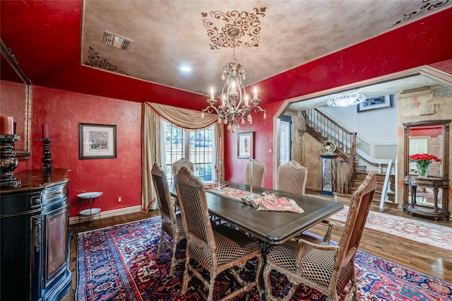 dining area with visible vents, baseboards, stairway, an inviting chandelier, and wood finished floors