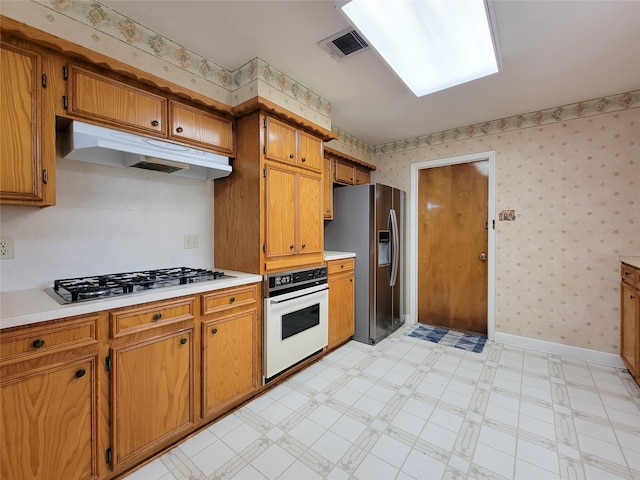 kitchen featuring white oven, stainless steel refrigerator with ice dispenser, and gas stovetop