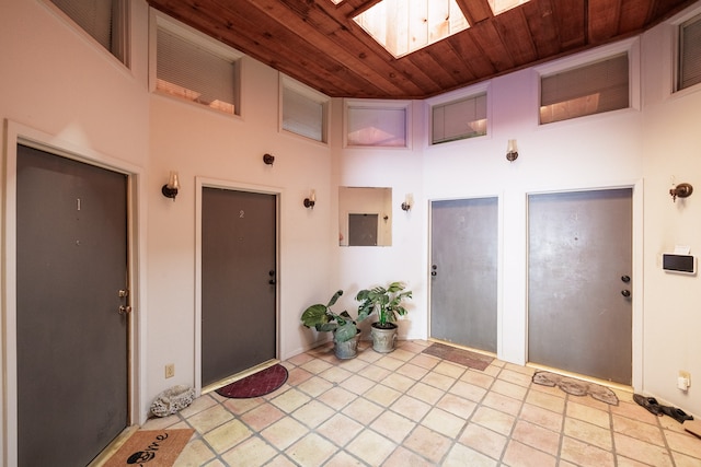 foyer with a skylight, light tile patterned flooring, wooden ceiling, and a high ceiling