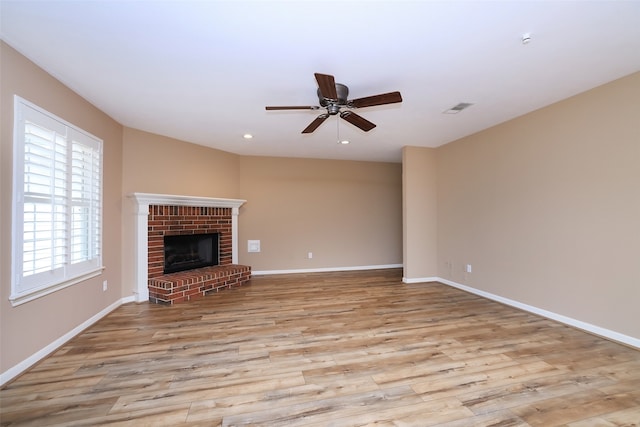 unfurnished living room featuring ceiling fan, light wood-type flooring, and a brick fireplace