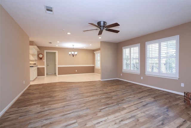 unfurnished living room with ceiling fan with notable chandelier and light wood-type flooring