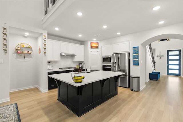 kitchen with a kitchen island with sink, light wood-type flooring, white cabinets, appliances with stainless steel finishes, and a kitchen bar