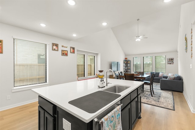 kitchen with light wood-type flooring, ceiling fan, a center island with sink, sink, and high vaulted ceiling