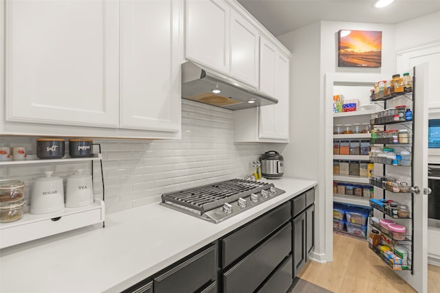 kitchen with stainless steel gas stovetop, light wood-type flooring, tasteful backsplash, and white cabinetry