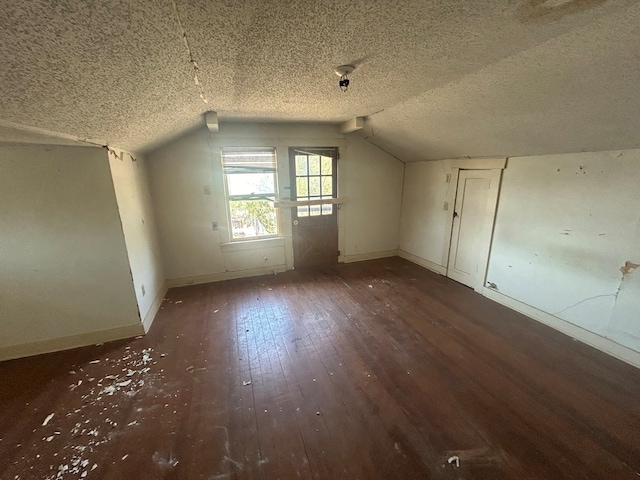 additional living space featuring dark hardwood / wood-style floors, a textured ceiling, and vaulted ceiling