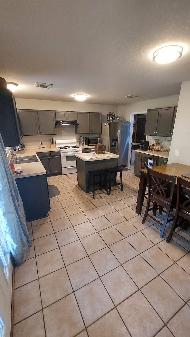 kitchen with sink, a center island, a breakfast bar, light tile patterned floors, and appliances with stainless steel finishes