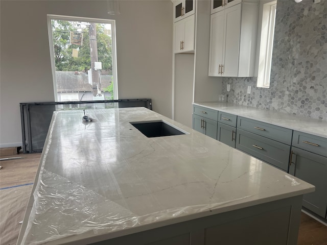 kitchen featuring tasteful backsplash, gray cabinets, light stone counters, and white cabinets