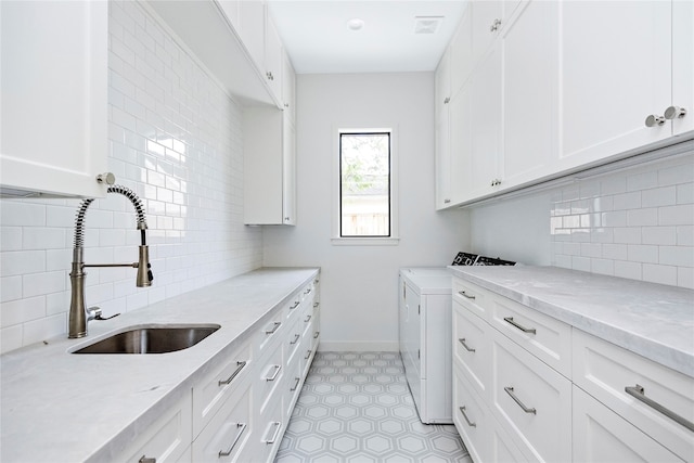 clothes washing area featuring washing machine and clothes dryer, sink, and cabinets