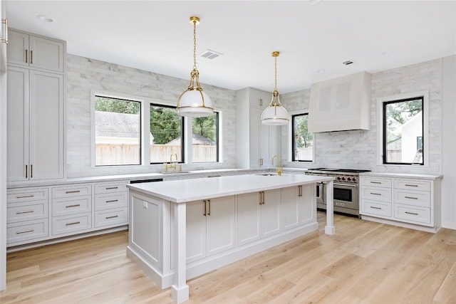 kitchen with hanging light fixtures, a kitchen island with sink, sink, and stainless steel stove