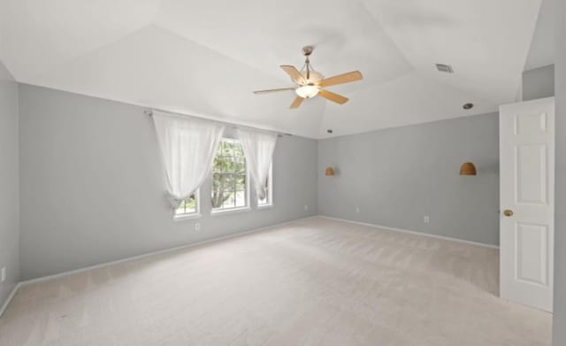 empty room featuring ceiling fan, vaulted ceiling, and light colored carpet