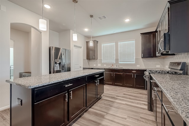 kitchen with decorative backsplash, a center island, light hardwood / wood-style floors, pendant lighting, and appliances with stainless steel finishes