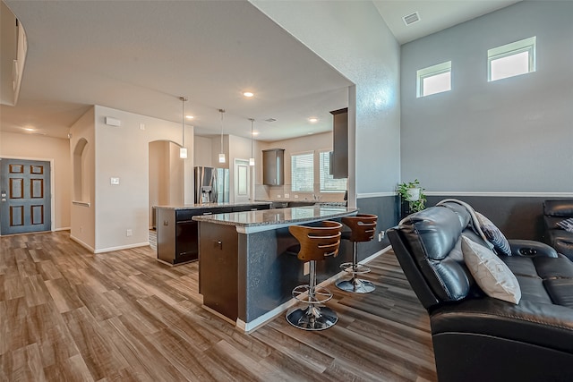 kitchen with light stone counters, wood-type flooring, stainless steel fridge, pendant lighting, and kitchen peninsula