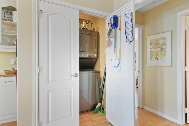 clothes washing area with baseboards, stacked washer and dryer, and light wood-style floors