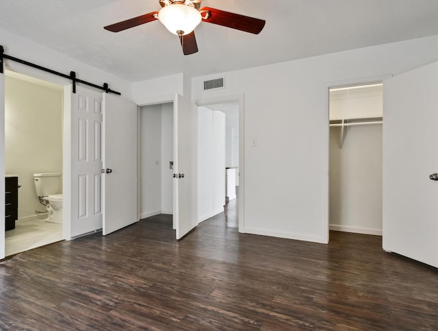 unfurnished bedroom with ceiling fan, ensuite bathroom, dark hardwood / wood-style floors, and a barn door