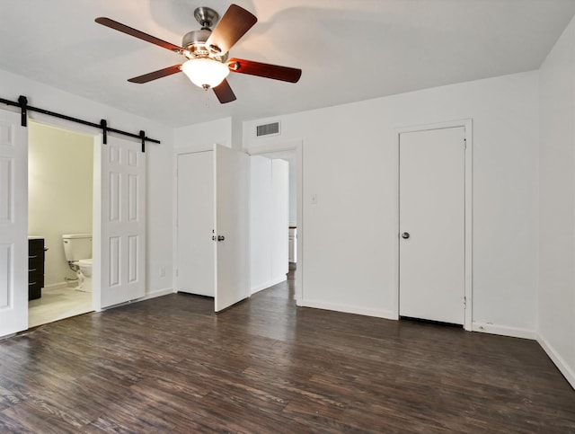 unfurnished bedroom featuring ceiling fan, a barn door, dark hardwood / wood-style floors, and ensuite bathroom