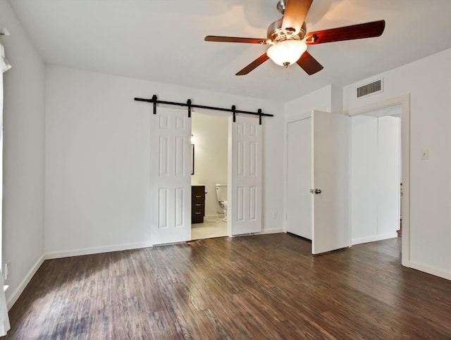 empty room with dark hardwood / wood-style flooring, a barn door, and ceiling fan