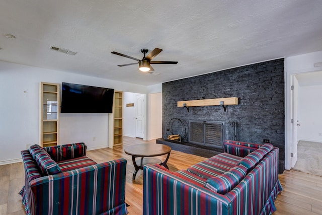 living room featuring ceiling fan, a large fireplace, a textured ceiling, and light wood-type flooring