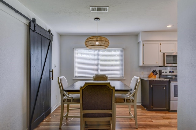 dining space with a barn door and light hardwood / wood-style flooring