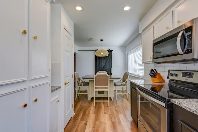 kitchen featuring hanging light fixtures, a barn door, light wood-type flooring, appliances with stainless steel finishes, and white cabinetry