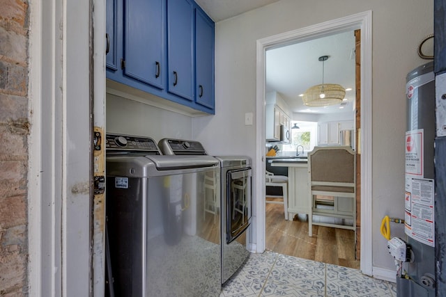 laundry area featuring sink, cabinets, gas water heater, light hardwood / wood-style flooring, and washer and clothes dryer