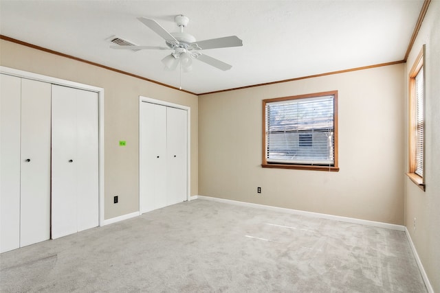 unfurnished bedroom featuring multiple closets, light colored carpet, and ceiling fan