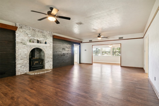 unfurnished living room with dark wood-type flooring, ceiling fan, a wood stove, and a textured ceiling