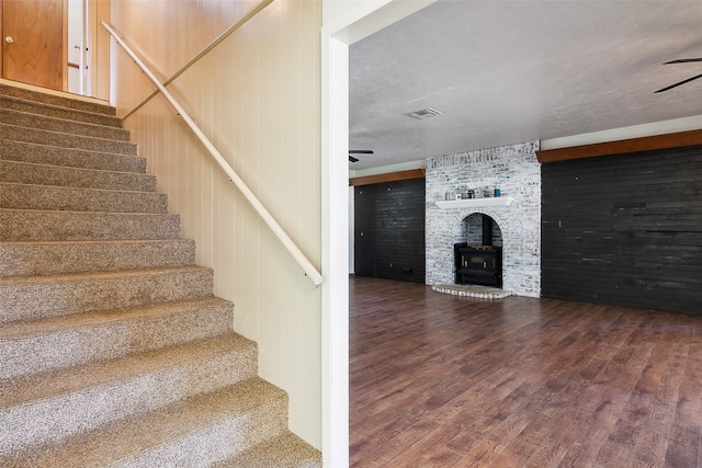 staircase featuring a wood stove, hardwood / wood-style floors, a textured ceiling, and wood walls