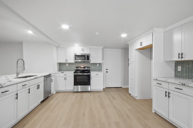 kitchen featuring sink, appliances with stainless steel finishes, light hardwood / wood-style floors, light stone counters, and white cabinetry