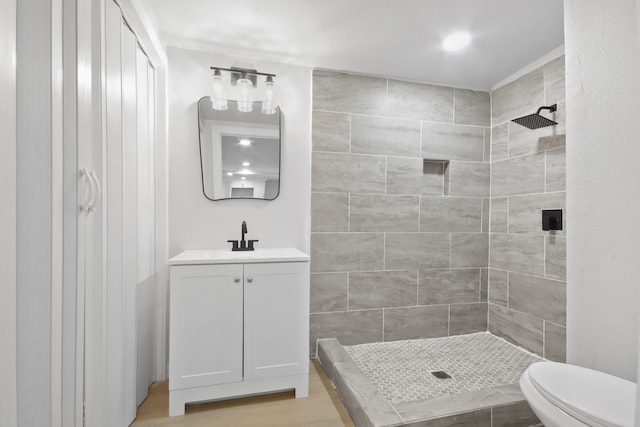 bathroom featuring hardwood / wood-style floors, vanity, toilet, and a tile shower