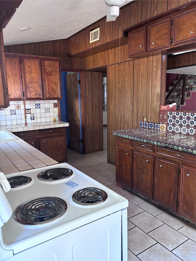 kitchen with wood walls, electric range, backsplash, and light tile patterned floors