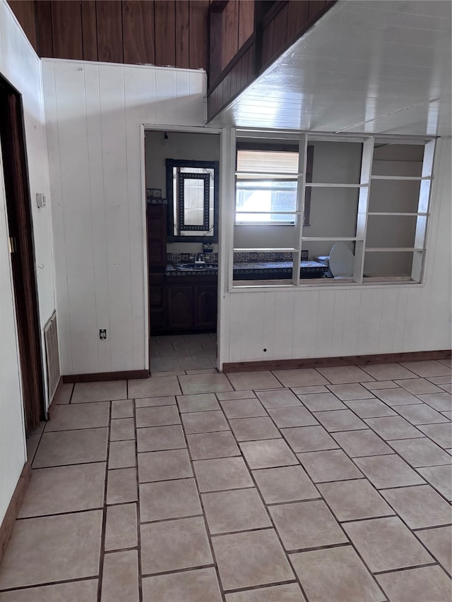 kitchen with light tile patterned flooring, wood walls, and sink