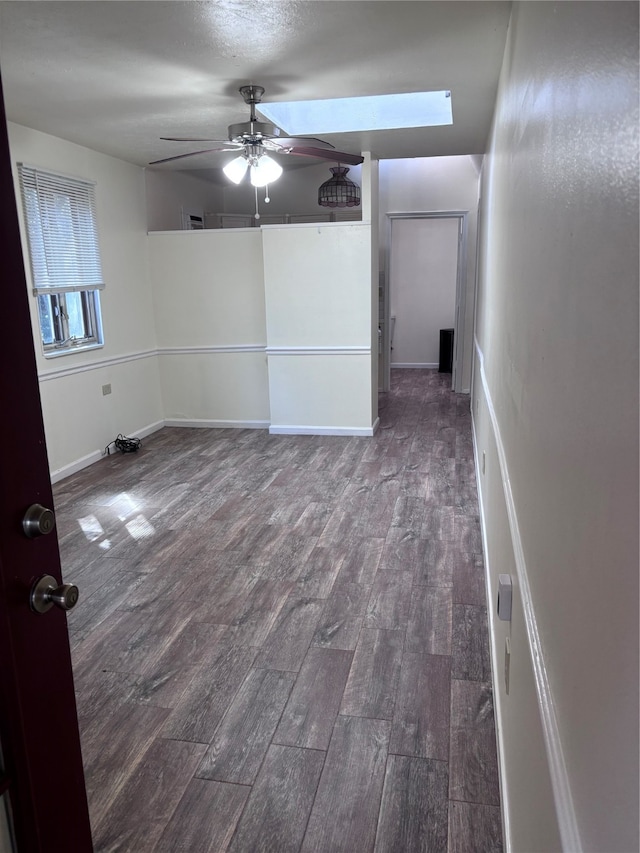 unfurnished room with a skylight, ceiling fan, and dark hardwood / wood-style floors