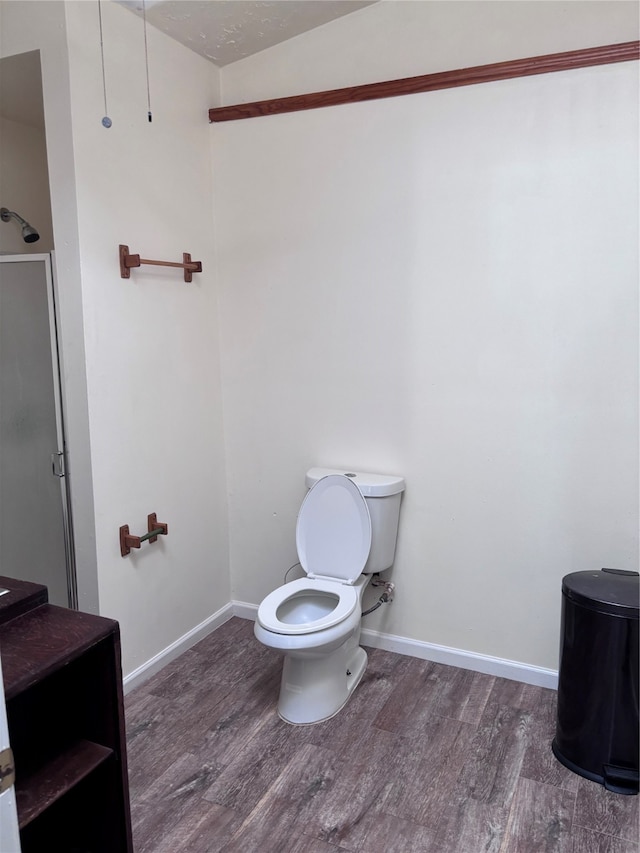 bathroom with vaulted ceiling, toilet, a shower with shower door, and hardwood / wood-style floors