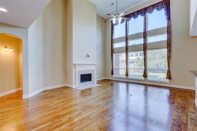 unfurnished living room featuring ceiling fan, a towering ceiling, and light wood-type flooring