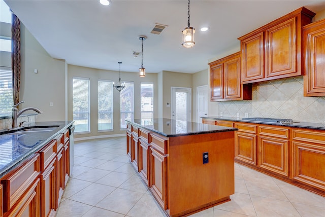 kitchen with decorative light fixtures, a kitchen island, dark stone countertops, and sink