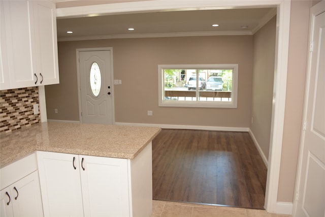 kitchen featuring light hardwood / wood-style flooring, light stone countertops, backsplash, white cabinets, and ornamental molding