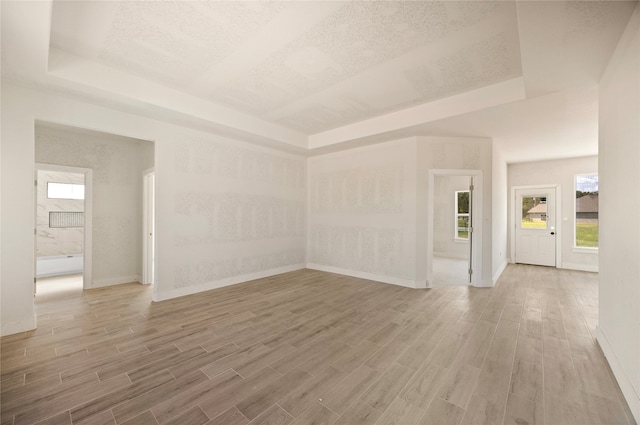 unfurnished room with a textured ceiling, wood-type flooring, and a raised ceiling