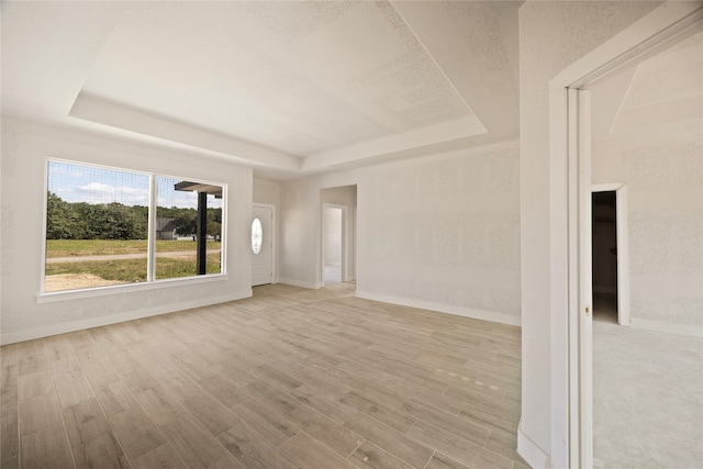 unfurnished living room featuring a tray ceiling and light hardwood / wood-style floors