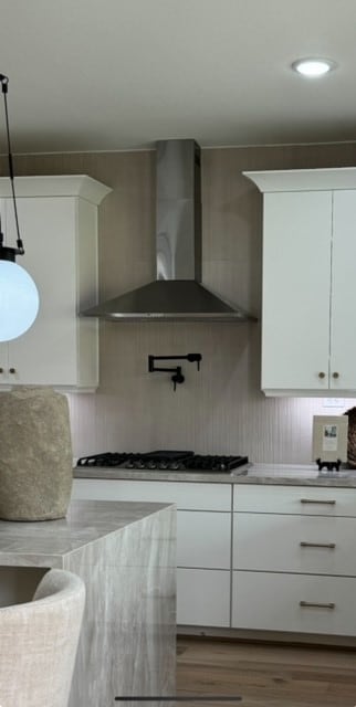 kitchen with pendant lighting, wall chimney exhaust hood, hardwood / wood-style flooring, and white cabinets