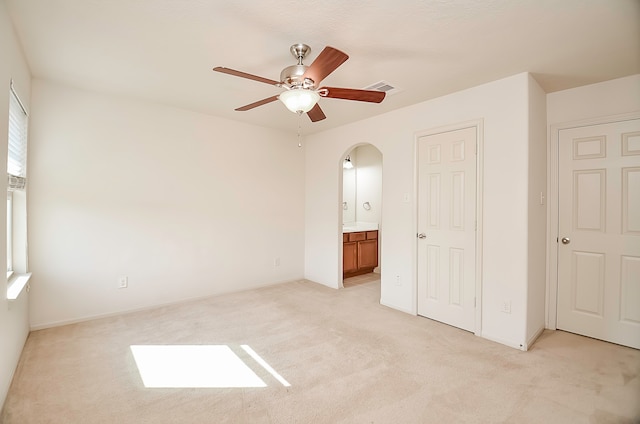 unfurnished bedroom with ceiling fan, light colored carpet, and ensuite bathroom